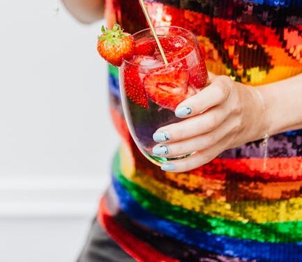 Person in vibrant sequin top holds a glass of strawberry cocktail.
