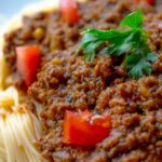 Close-up of a tasty spaghetti Bolognese topped with fresh parsley and tomatoes.