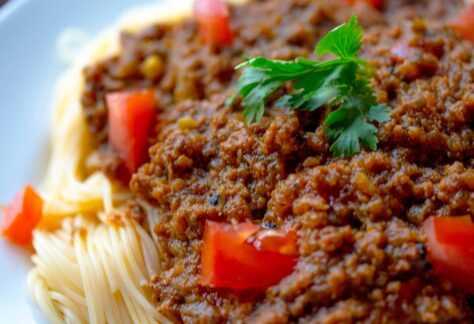 Close-up of a tasty spaghetti Bolognese topped with fresh parsley and tomatoes.