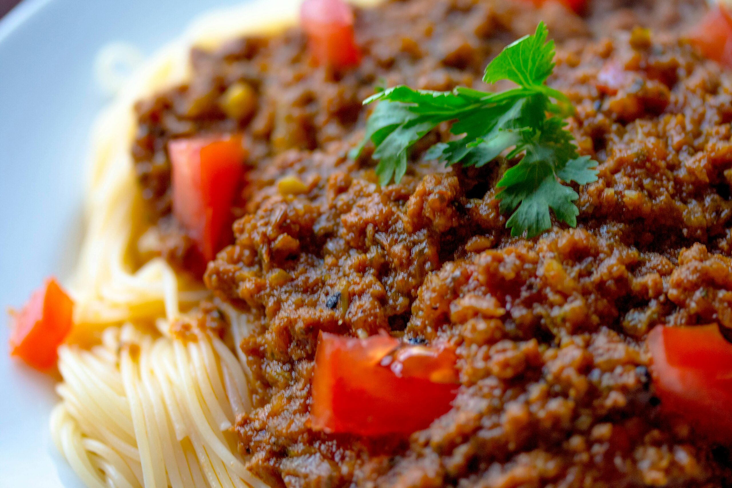 Close-up of a tasty spaghetti Bolognese topped with fresh parsley and tomatoes.