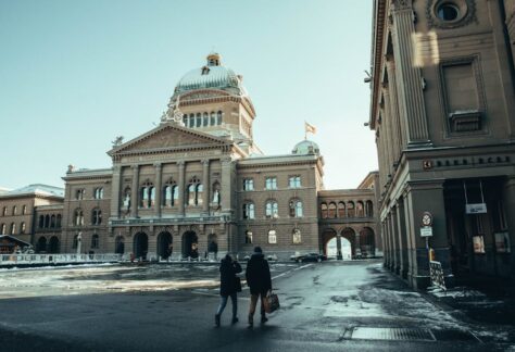 A couple walks in front of the Swiss Parliament Building in Berne, capturing a winter urban scene.